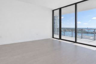 Luxury Home Staging Before-After -Modern room with large glass doors leading to a balcony with a view of water and buildings.