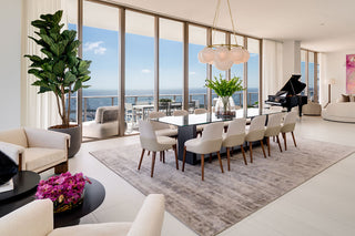 Luxury Home Staging Before-After -Modern living room with a dining table, chairs, and a piano by a large window with a view of the ocean.