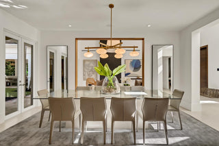 Turnkey Furniture Packages for purchase. Modern dining room with a glass table and chairs, featuring a chandelier and large windows. All About the Wow