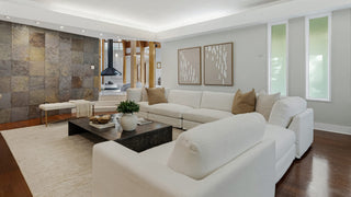 Home Staging and Turnkey Furniture Rental - A modern living room featuring a large white sectional sofa with beige and white throw pillows, a black rectangular coffee table, a cream area rug, and a textured stone accent wall in the background.